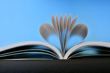 Páginas de un libro curvadas en forma de corazón, aislado sobre fondo azul