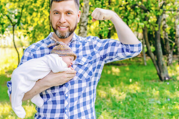 Naklejka na ściany i meble Happy smiling young bearded father with a newborn baby in his arms in the park on a sunny summer day