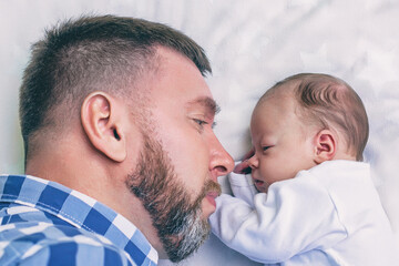 happy young bearded father with newborn baby lying in bed face to face