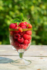ripe raspberries in a glass on a green background on a Sunny day