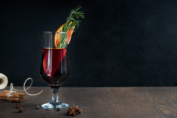 Glass of hot spiced red mulled wine usually prepared on christmas holidays decorated with orange slices and rosemary on front of cinnamon bunch and anice star on wooden table. Image with copy space