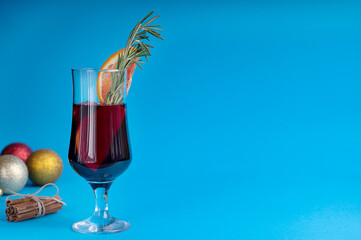 Side view of a glass of red mulled wine usually prepared at winter on christmas eve decorated with orange sliced and fresh rosemary in front of cinnamon bunch. Image with copy space
