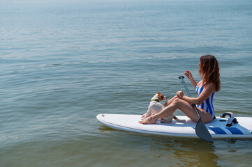 A woman is riding a sup surfboard with a dog on the lake. The girl goes in for water sports with her pet.