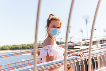 A beautiful young woman in mask is looking seriously through the gates on a summer sunny day