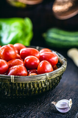 small red organic tomato, fresh vegetable used in Brazilian cuisine. dark straw basket with farm food