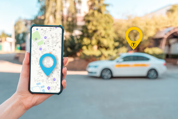 A woman holds a cellphone with an online map app, hand close-up. In the background is a city street with taxi car. The concept of online navigation and modern technologies