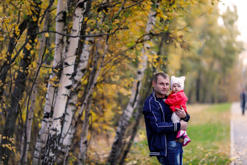 Child in arms of man's father. Autumn day. Pretty, happy, blue-eyed one-year-old girl in red coat and white hat. Charming baby shows emotions close-up. Concept of healthy child and parenting