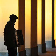 Silhouette of an accordion player in Italy against yellow columns light by a warm sunlight. Square...