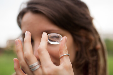 Young beautiful girl with dreadlocks holds in hand rhinestone, transparent quartz, natural stone outdoors during morning near her face