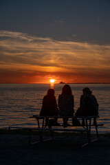 Fototapeta na wymiar Silhouettes of three women sitting on a bench watching the sunset over the ocean in Sweden