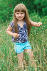 Little girl with long hair walks on the grass at the edge of the forest