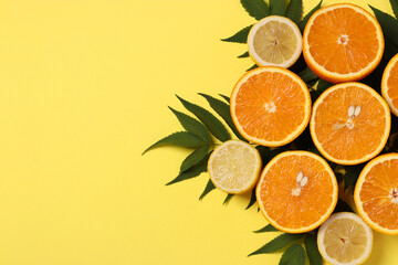 Composition of halves of lemons and oranges with green leaves on a bright yellow background, View...