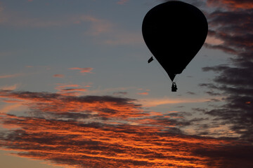 Dark silhouette of a hot air ballon floating over clouds illuminated orange in the sunset