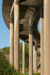View from under a concrete bridge. Water is reflecting from the sea unto the pillars in the evening sun. The photograph is shot in portrait orientation. The bridge is slightly curved to the right.