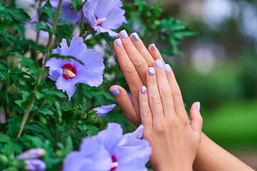 Female manicure with color nail polish and silver glitter against the background of flowers in a park outdoors