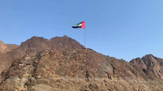 United Arab Emirates flag waving on top of a hill in the Middle of 
Hatta lake on blue sky background. Beautiful UAE flag. National UAE symbol, national day. 