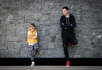 Confident father and son with arms crossed against the wall.