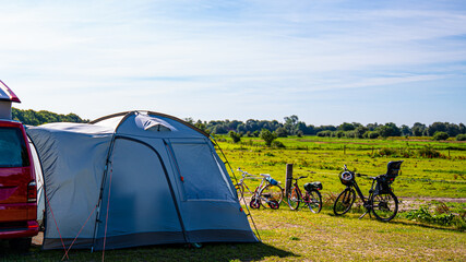 Tourist tents and car in green field at campsite. Camping place in the meadow in nature park in...