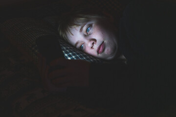 Depressed Teen Girl Lying down on a bed while using her smart phone at night