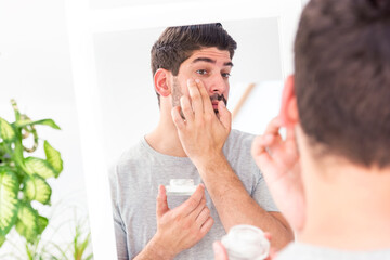 Man applying cream onto his face while standing in the bathroom
