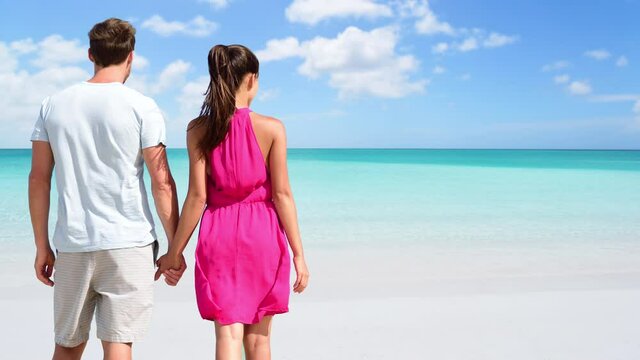 CINEMAGRAPH - SEAMLESS LOOP: Summer holidays - couple on tropical beach vacation standing in white sand relaxing looking at ocean. Romantic young adults holding hands in love. Looping Motion photo