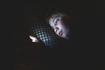 Depressed Teen Girl Lying down on a bed while using her smart phone at night