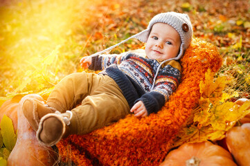 Child boy lies in a basket with pumpkins in autumn leaves.
