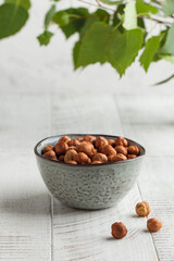 A handful of hazelnuts in a grey bowl on a white wooden background. Healthy snacks. Nuts.