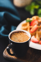 Cup of espresso coffee with sweet belgian waffles on background. Closeup view selective focus