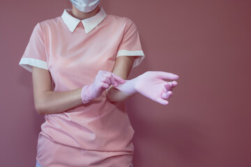 A girl in a medical mask puts on pink disposable gloves before the procedure