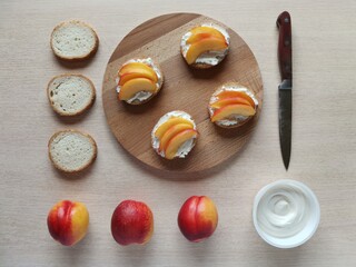  sandwiches with cream cheese, fresh nectarines slices on a serving wooden plank and ingredients. 