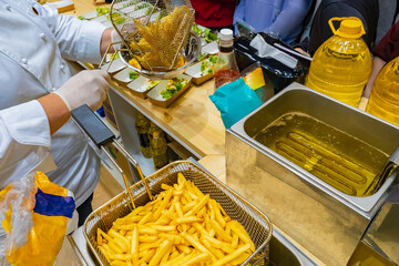 Cooking French fries in a fast food restaurant. Cook fried potato slices in boiling oil. Industrial deep fryer. Serving potatoes and salad. Snack. Garnish.