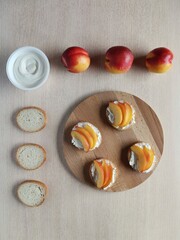 Bright sandwiches with cream cheese, fresh nectarines slices on a serving plate wooden plank. 