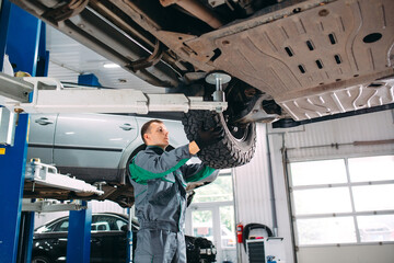 Car lifted in automobile service for fixing, worker repairs the wheel,