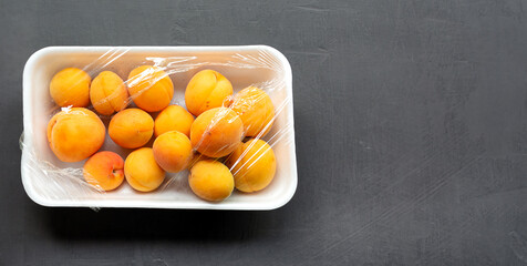 Apricots on a plastic plate, covered with plastic wrap on a gray background. Copy space