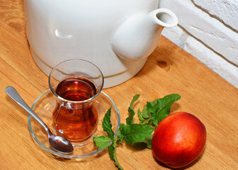 Glass of tea, teapot, peach and mint sprig close up