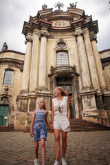 Mother and daughter walk together cheerfully in historic square of old tourist town