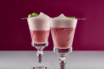 zwei pinke Cocktail Getränke mit grünen Apfel Spießen in alten Kristall Gläsern auf weißer reflektierender Oberfläche mit pinkem Hintergrund