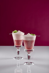 zwei pinke Cocktail Getränke mit grünen Apfel Spießen in alten Kristall Gläsern auf weißer reflektierender Oberfläche mit pinkem Hintergrund