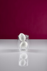 zwei Eier im Glas auf weißer reflektierender Oberfläche mit pinkem Hintergrund