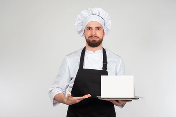 The chef makes an inviting gesture with his hand and smiles. The chef points to a placard with place for text. Advertising for the restaurant. The cook invites you to the cafe.