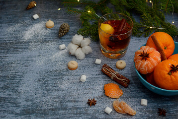Christmas composition of tangerines in a blue bowl, cinnamon sticks, marshmallows, glasses with tea, spruce branches and garlands.