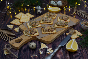 Appetizing crackers with paste on a cutting board, lemon slices and a knife on table.