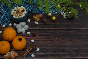Tangerines, spruce branches, marshmallows, garlands, cinnamon sticks in the form of a Christmas composition on a dark wooden background.