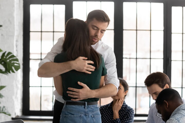 Upset man and woman hugging at group therapy session, overcoming problem together, depression or...