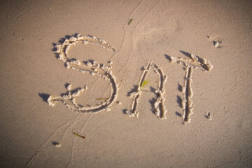Sat. for Saturday, written on beach sand