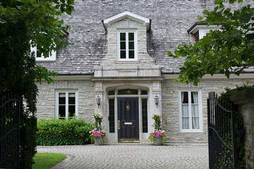 Elegant gated entrance to stone house  with dormer window and cedar shingle roof