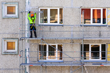 the worker assembles the scaffolding on the facade of a multi-storey house at a dangerous height