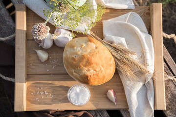 Still life of bread, wheat, garlic and salt on a wooden box in natural conditions in nature. The concept of farm products, natural food, cooking with your own hands, the unity of man with nature.
