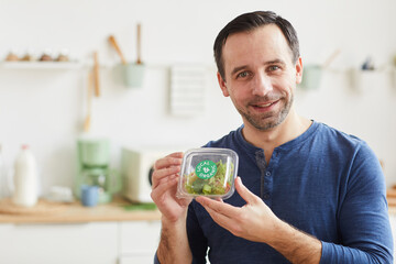 Portrait of mature bearded man holding salad box and smiling at camera while enjoying food delivery service, copy space